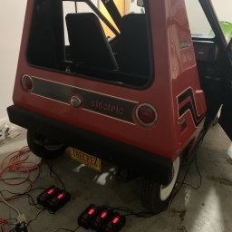 The back of a CitiCar with five battery chargers below it lighted up in red.